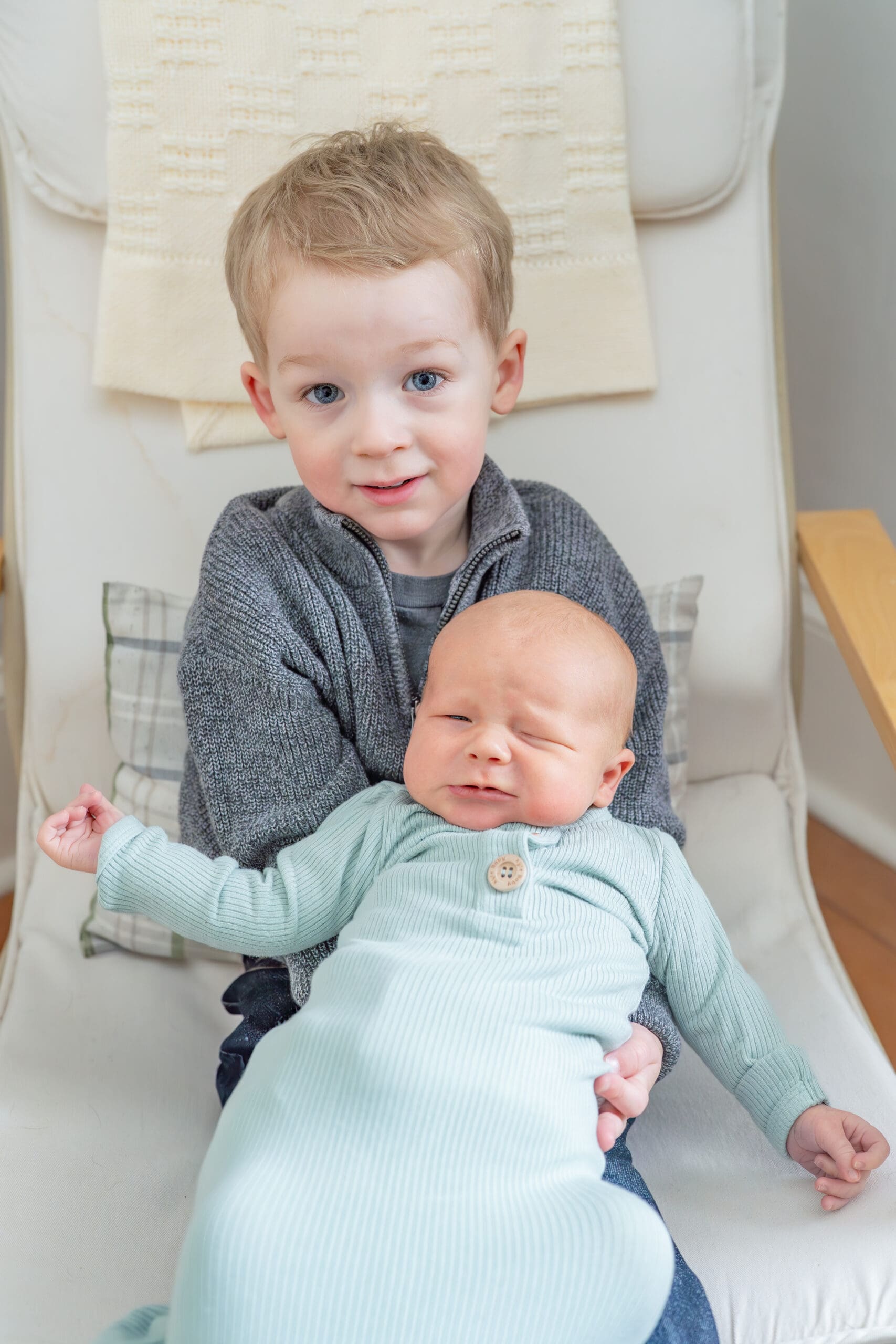 Big brother holding new baby brother on recliner — photographed by Alliston and Barrie maternity, newborn, and family photographer.