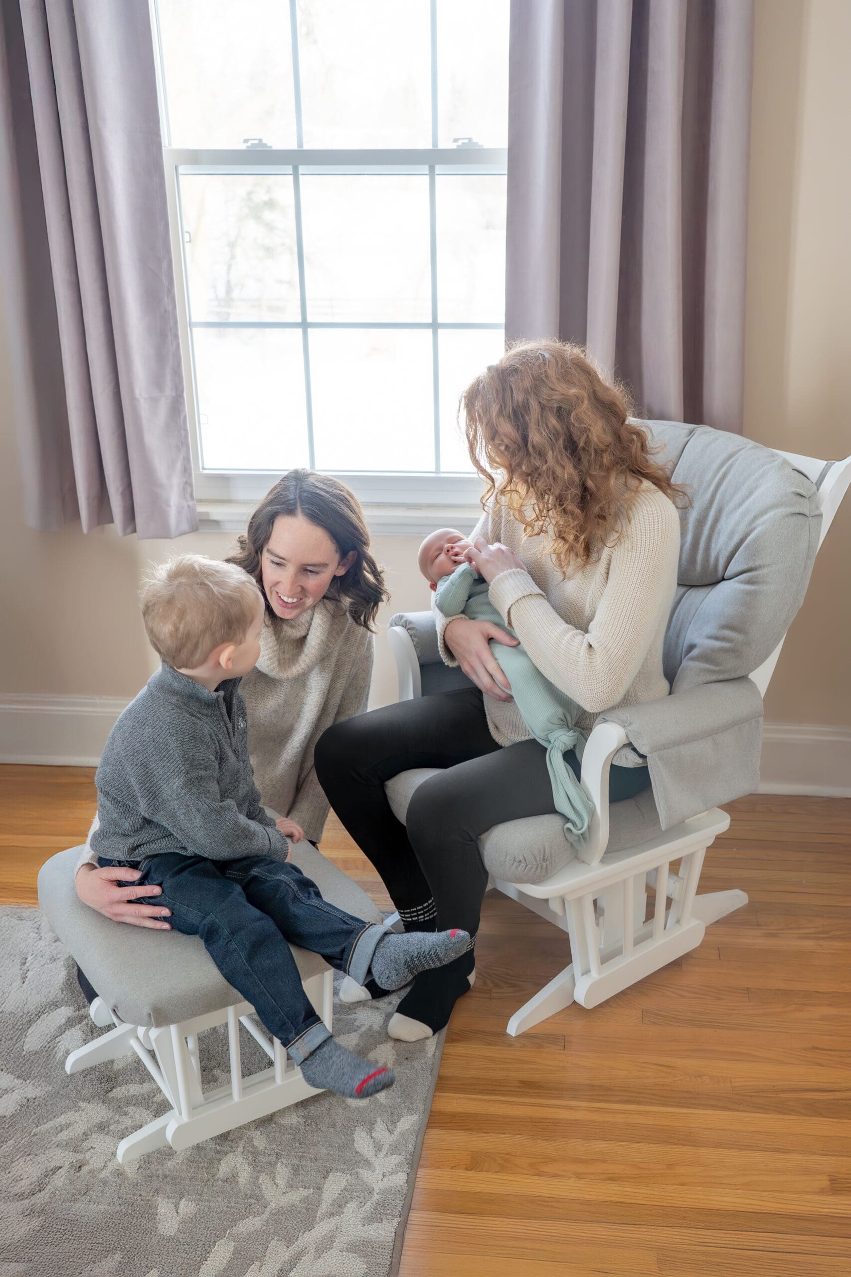 Lifestyle newborn photography session with two moms reading to toddler and holding baby in cozy nursery with natural light  — photographed by Alliston and Barrie maternity, newborn, and family photographer.