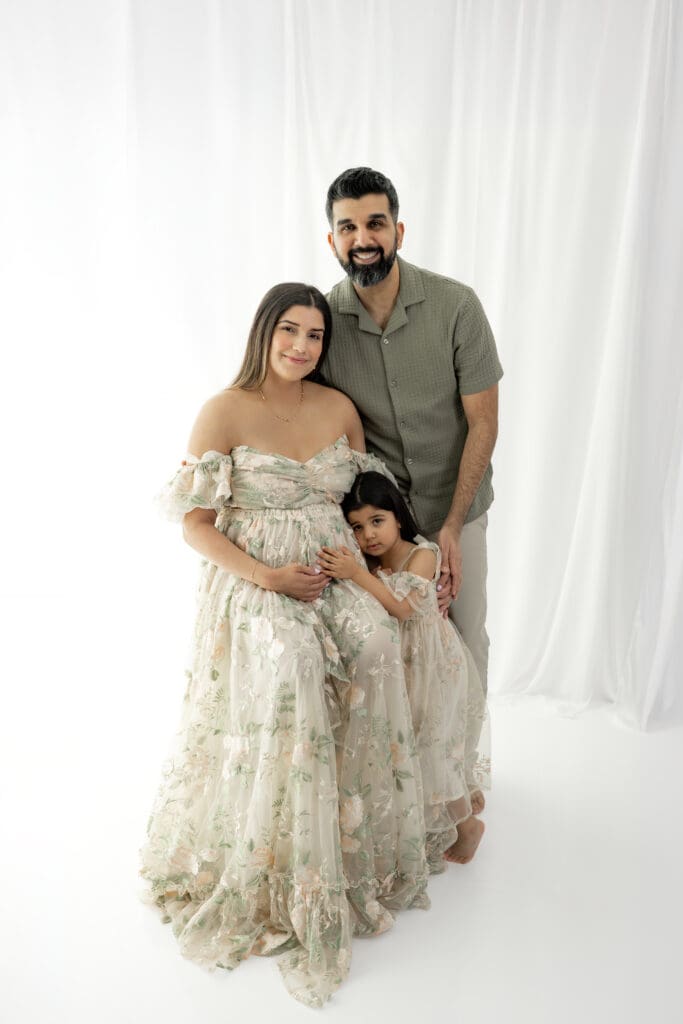 Expecting family smiling at camera during a soft, natural light maternity session — photographed by Alliston and Barrie maternity, newborn, and family photographer.