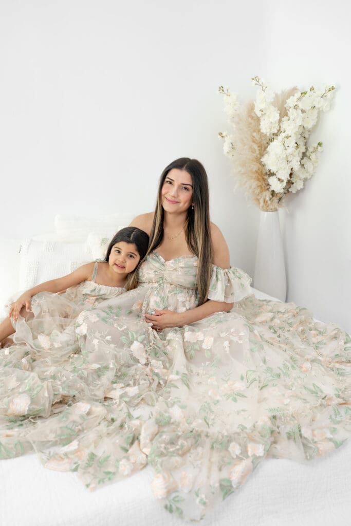 Expecting mother hugging toddler in matching floral gowns during a soft, natural light maternity session — photographed by Alliston and Barrie maternity, newborn, and family photographer.
