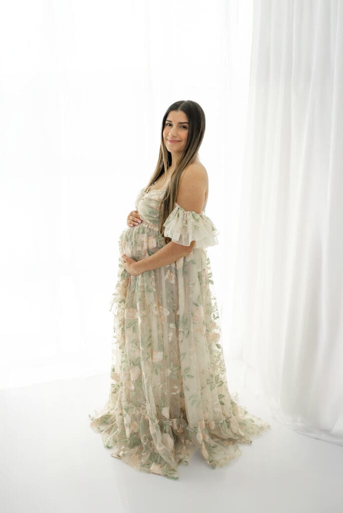 Expecting mother in floral gown smiling during a soft, natural light maternity session — photographed by Alliston and Barrie maternity, newborn, and family photographer.