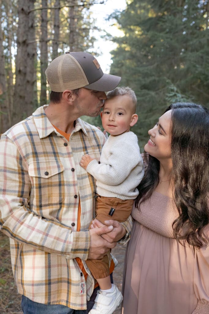 Dad kissing toddler while mom looks on during family photography session in Bradford