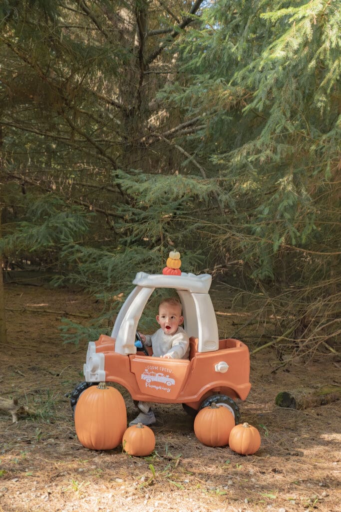 Toddler sitting in orange car with pumpkins surrounding him during family photography session in Bradford