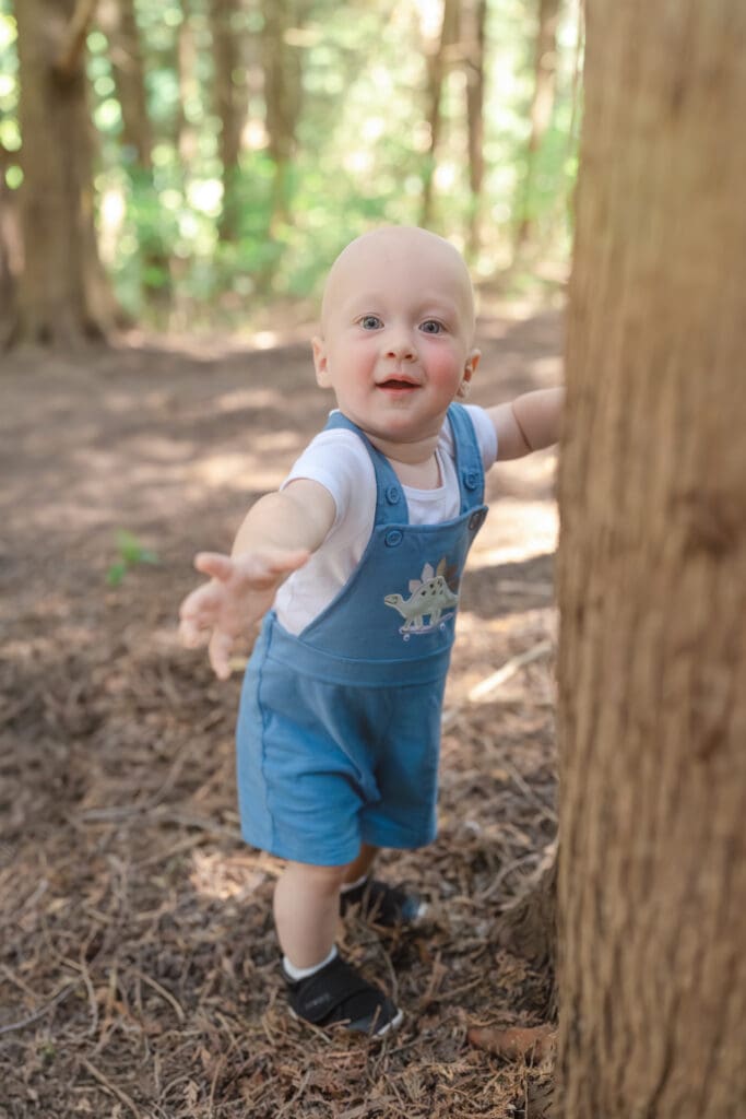 Toddler standing while holding onto tree trunk during family photography session in Tottenham