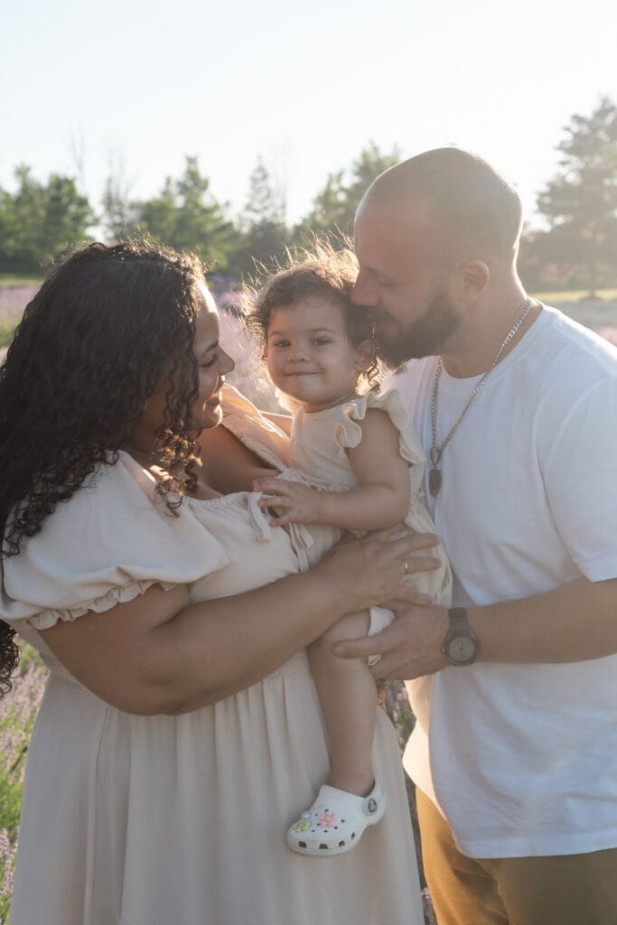Parents hugging toddler in lavender field during family photography session in Creemore