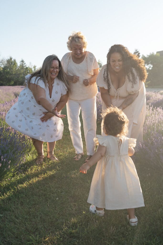 Mom and grandmas smiling at toddler in lavender field during family photography session in Creemore