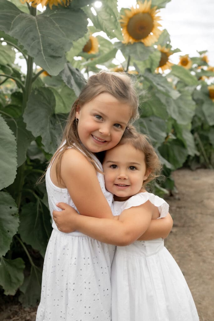 Sisters hugging in sunflower field during family photography session in Innisfil