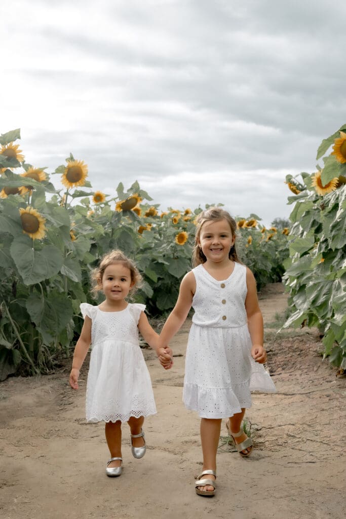 Sisters walking and holding hands in sunflower field during family photography session in Innisfil