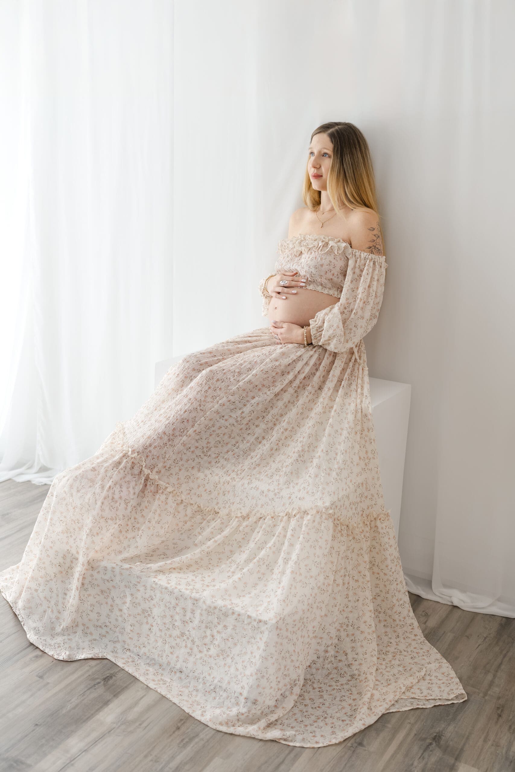 Fine art maternity session in Barrie featuring mom in two-piece gown sitting on stairs and holding bump