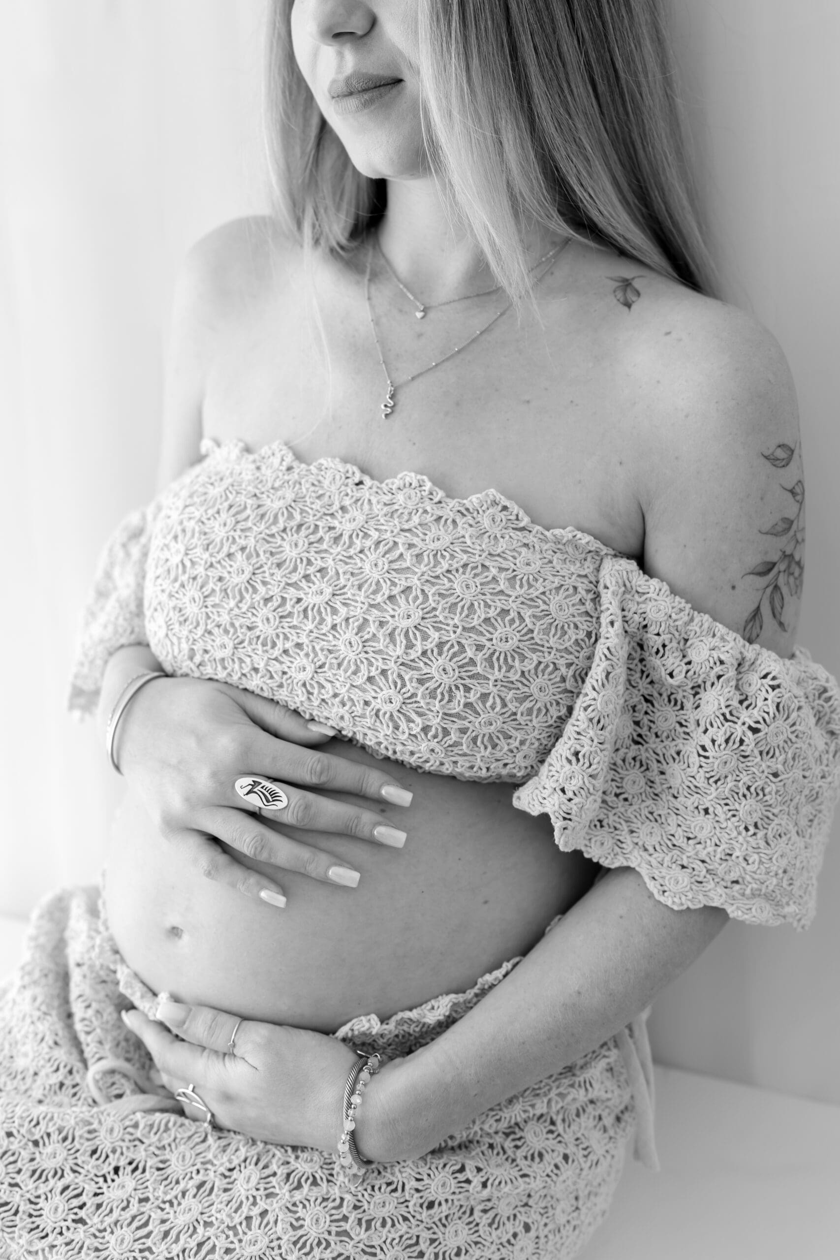 Fine art Barrie maternity session featuring woman sitting on bed in two-piece gown holding bump
