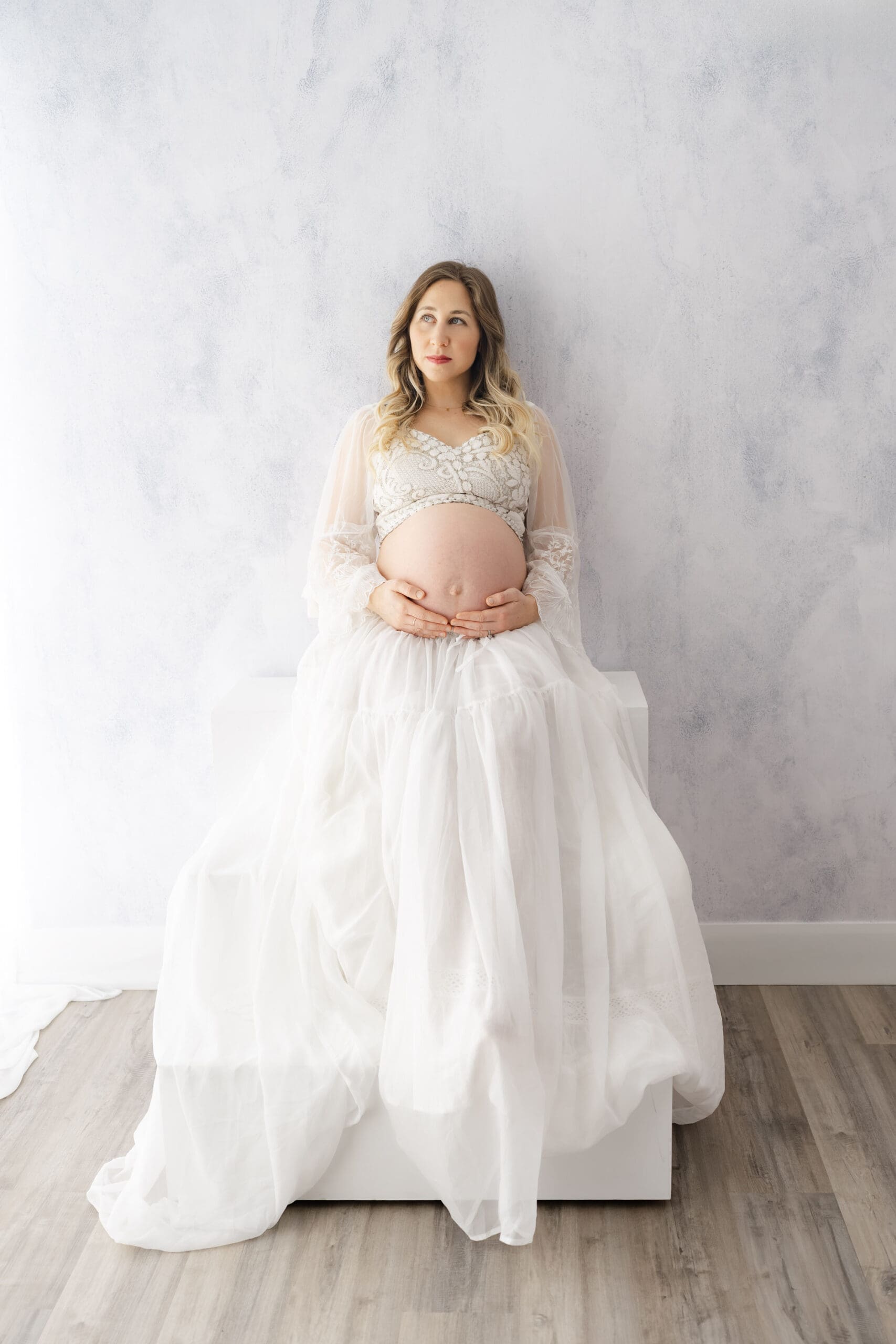 Fine art Barrie maternity session featuring woman sitting on stairs and holding bump 