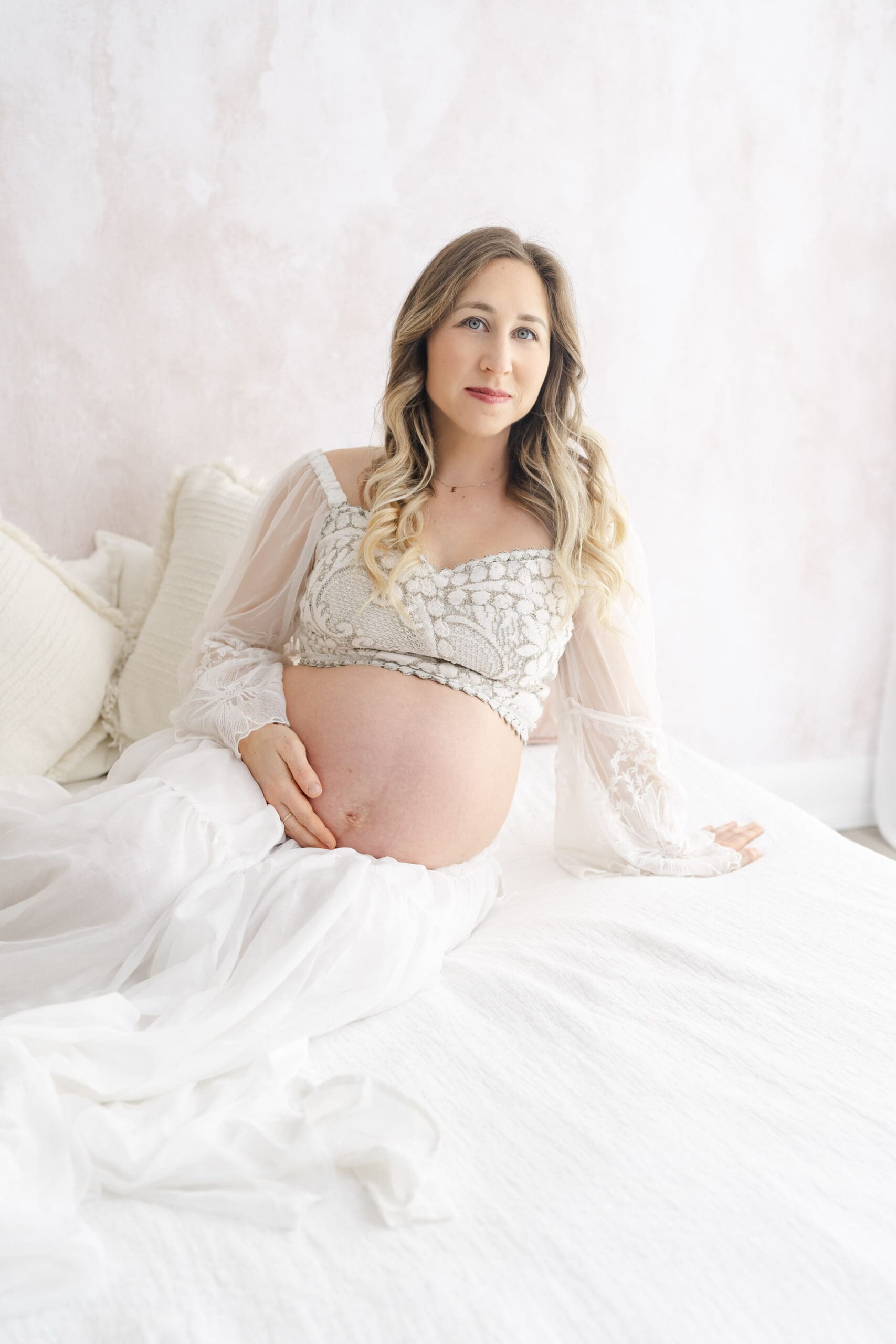 Fine art Barrie maternity session featuring woman sitting on bed and holding bump 