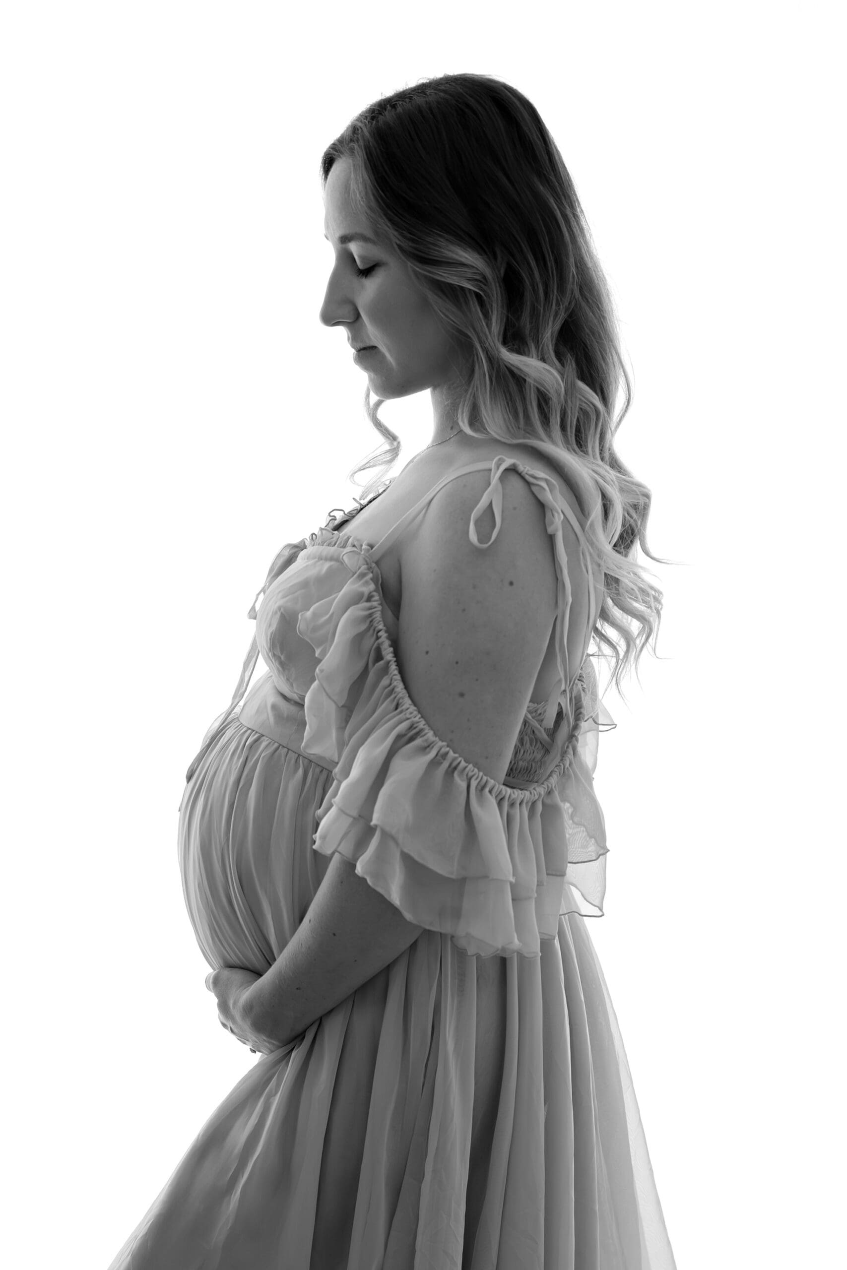 Fine art Barrie maternity session featuring black and white silhouette of woman holding bump with eyes closed
